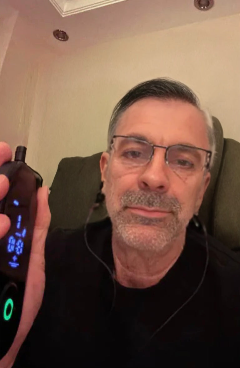 NeuroRest-Man holding a digital device with a screen, sitting in a chair indoors.
