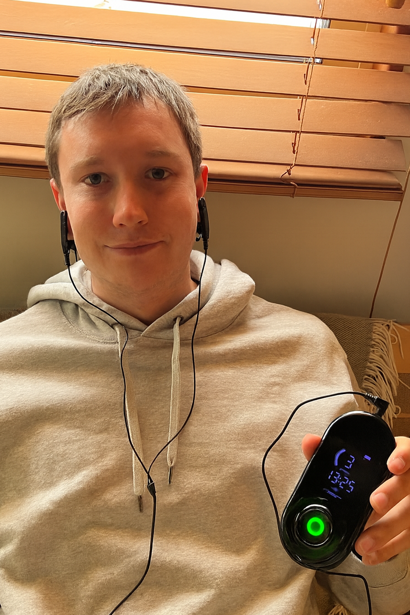 NeuroRest-Person wearing headphones holding a digital device with a green light.